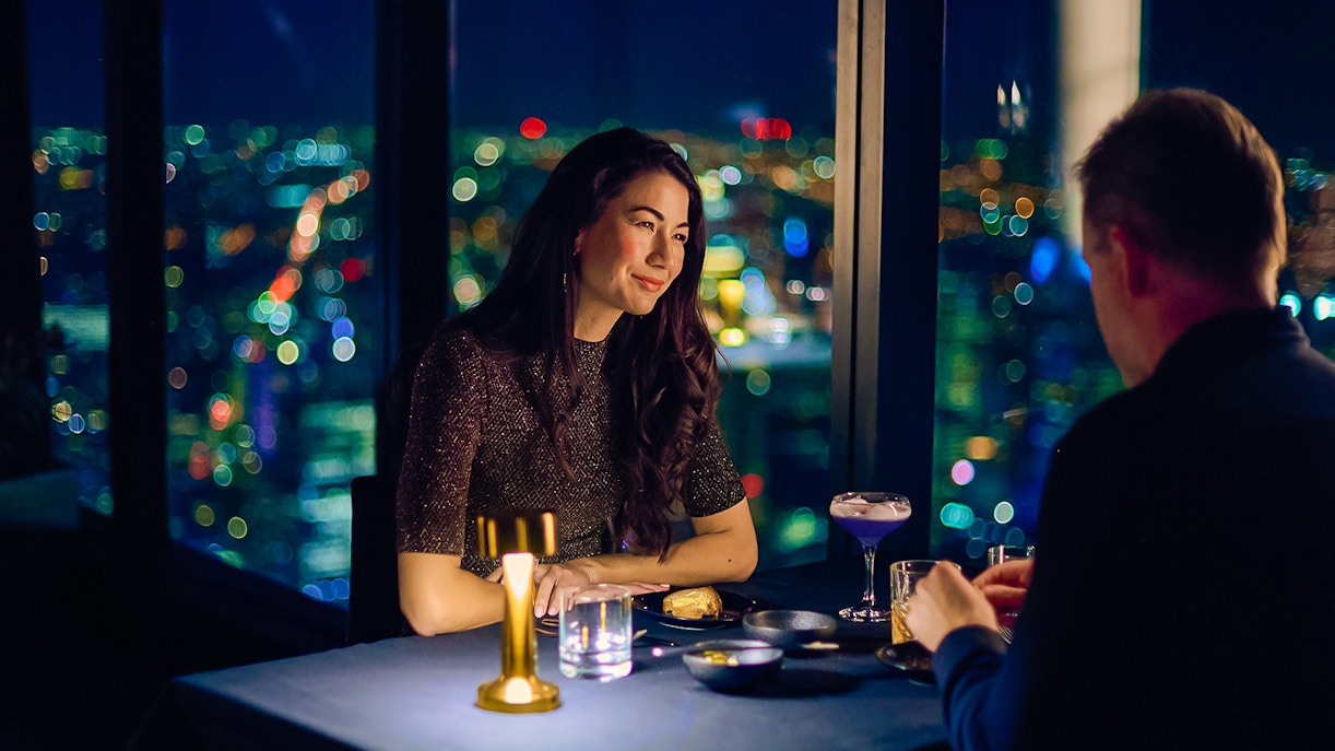 Couple dining at Altitude experience, Melbourne Skydeck with city lights in background.