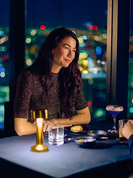 Couple dining at Altitude experience, Melbourne Skydeck with city lights in background.