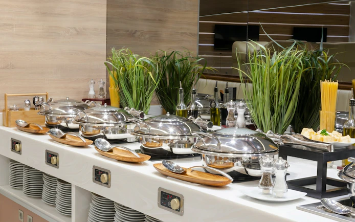 Buffet setup at MERA Business Lounge, Cancun Airport, featuring chafing dishes and condiments.