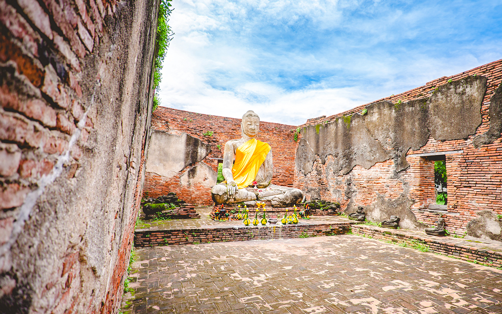 Seated Buddha statue in Wat Lokayasutharam, Ayutthaya, surrounded by ancient brick walls.