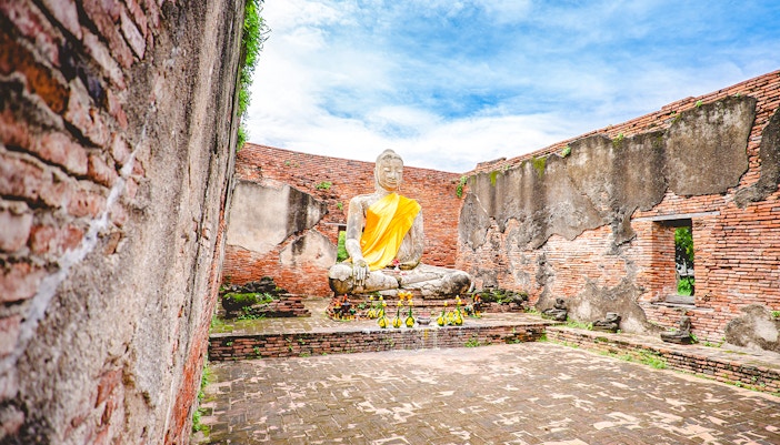 Seated Buddha statue in Wat Lokayasutharam, Ayutthaya, surrounded by ancient brick walls.