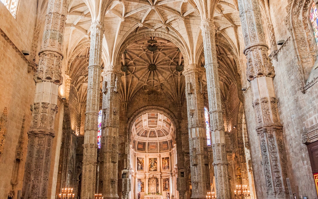 Interior of Jerónimos Monastery in Lisbon with ornate columns and vaulted ceilings.