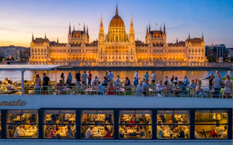 Cruise guests enjoying views of the illuminated Hungarian Parliament Building on the Danube River in Budapest.