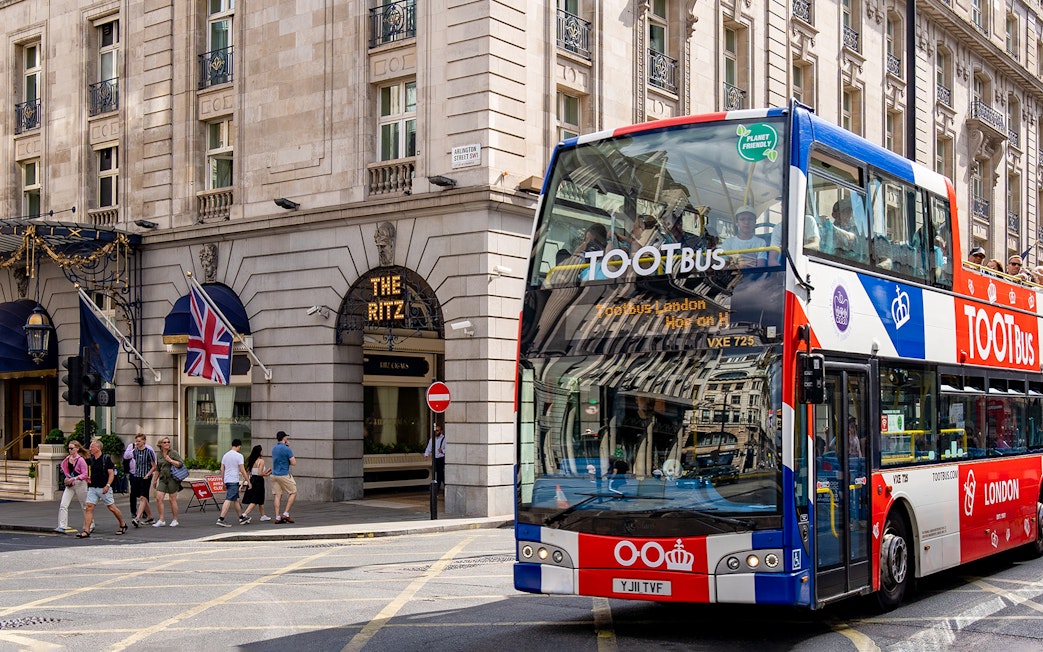 Tootbus passing The Ritz in London with passengers on a sunny day.