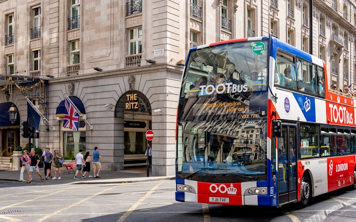 Tootbus passing The Ritz in London with passengers on a sunny day.