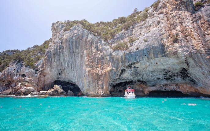 Boat entering Grotta del Bue Marino cave near Cala Luna beach, Sardinia.