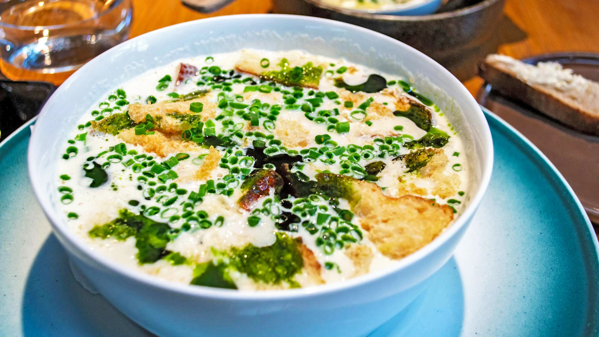 Traditional Norwegian fish soup with creamy broth, fish fillet, bread, and scallions in a white bowl.