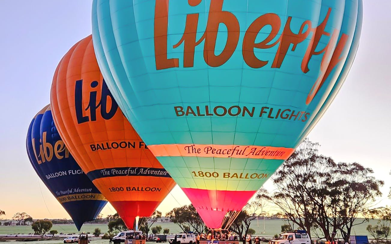 Liberty hot air balloons preparing for flight at sunrise in open field.
