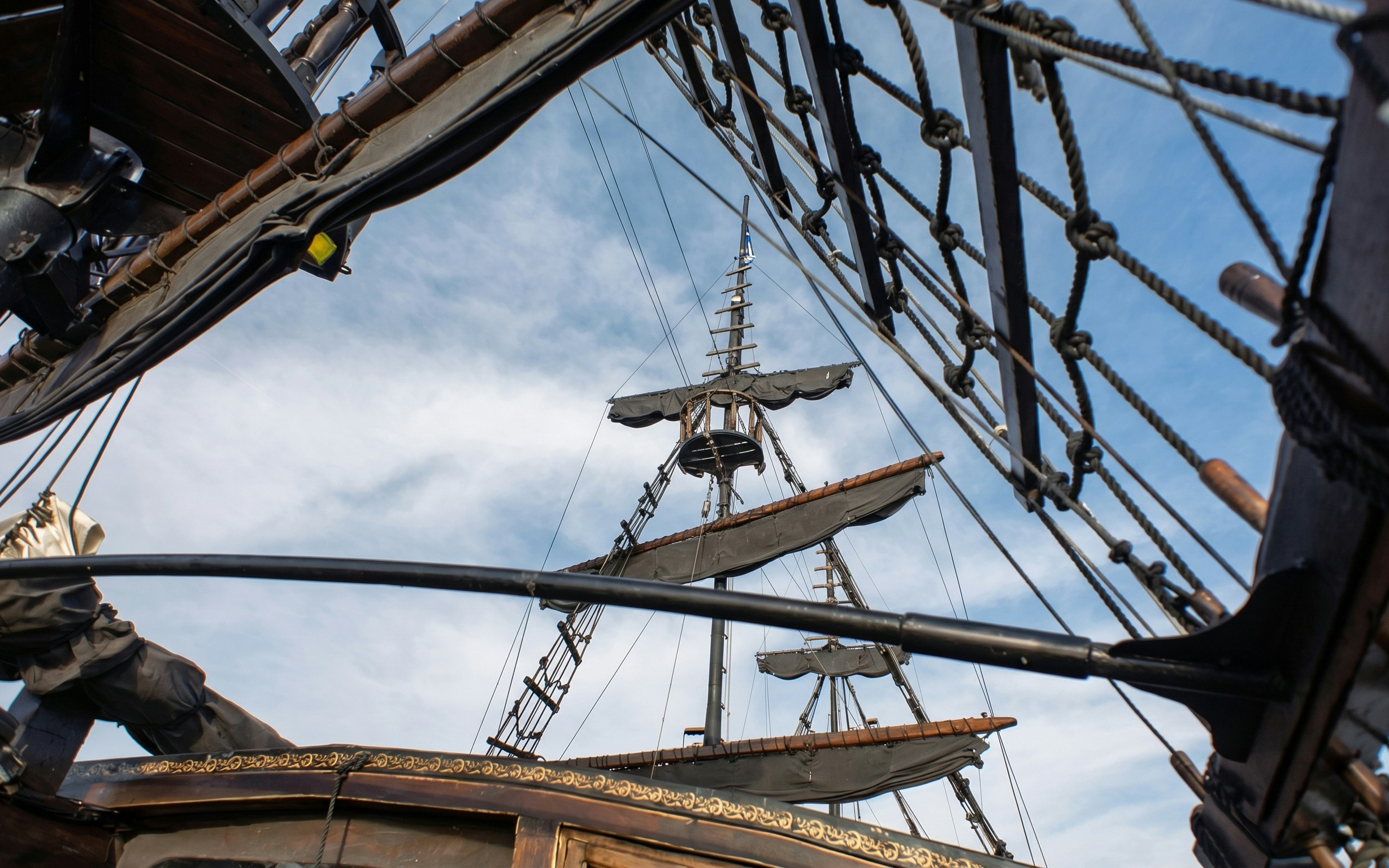 Pirate ship mast with sails, ropes, and ladders against a blue sky.