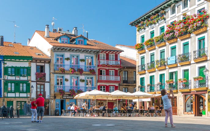 Colorful buildings and outdoor café in Hondarribia, Spain, with people enjoying the plaza.