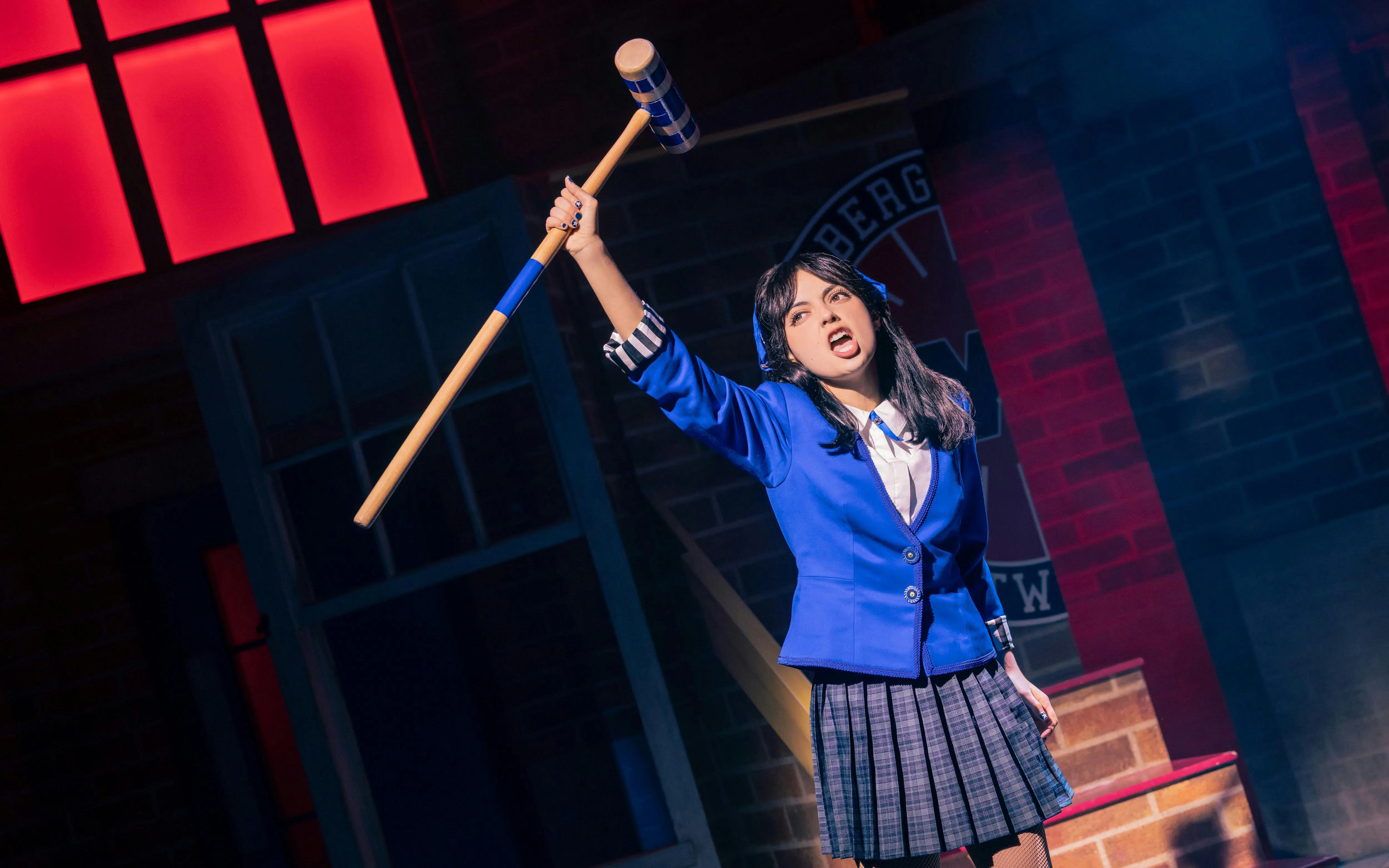 Performer in blue blazer holding croquet mallet during Heathers The Musical scene.