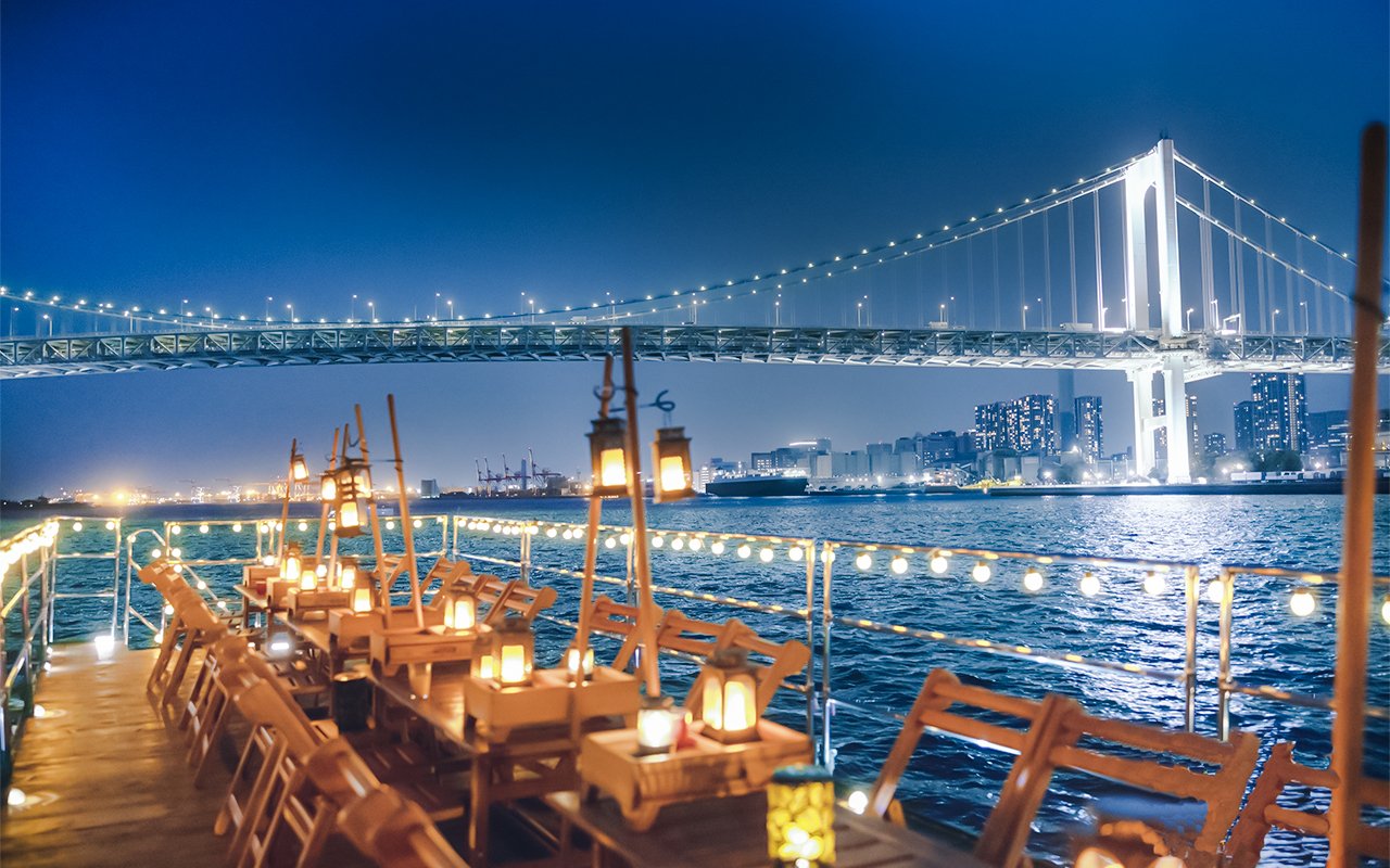 Night view from Yakatabune Cruise deck with illuminated bridge and city skyline in background.