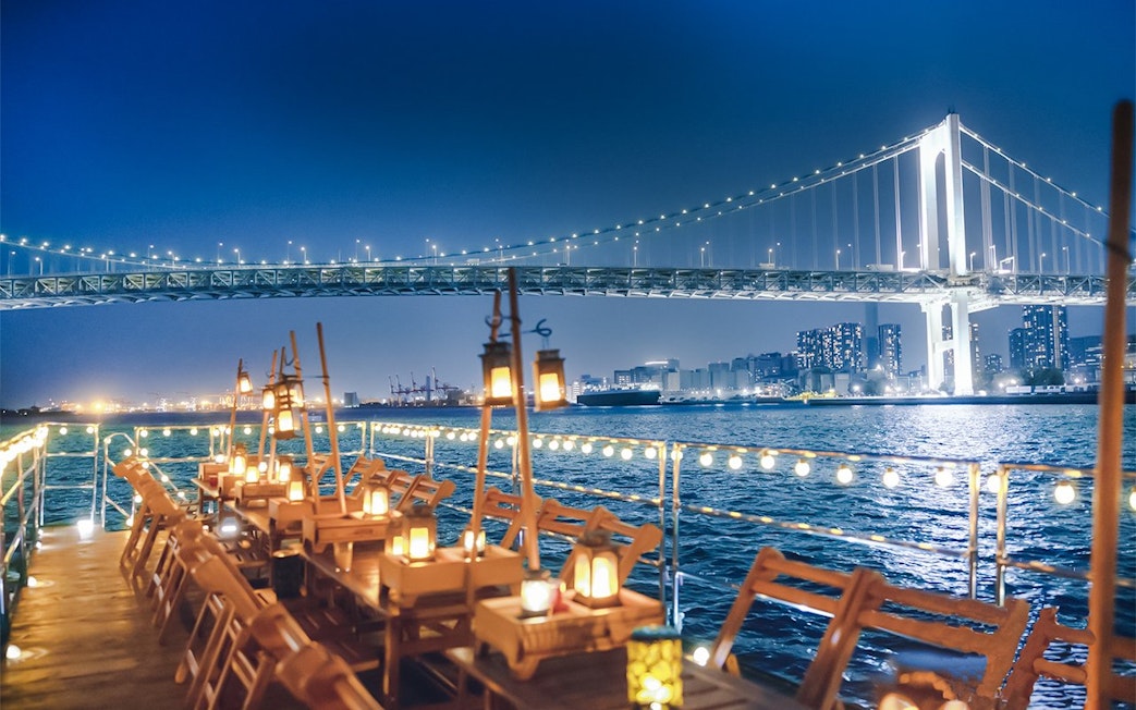Night view from Yakatabune Cruise deck with illuminated bridge and city skyline in background.