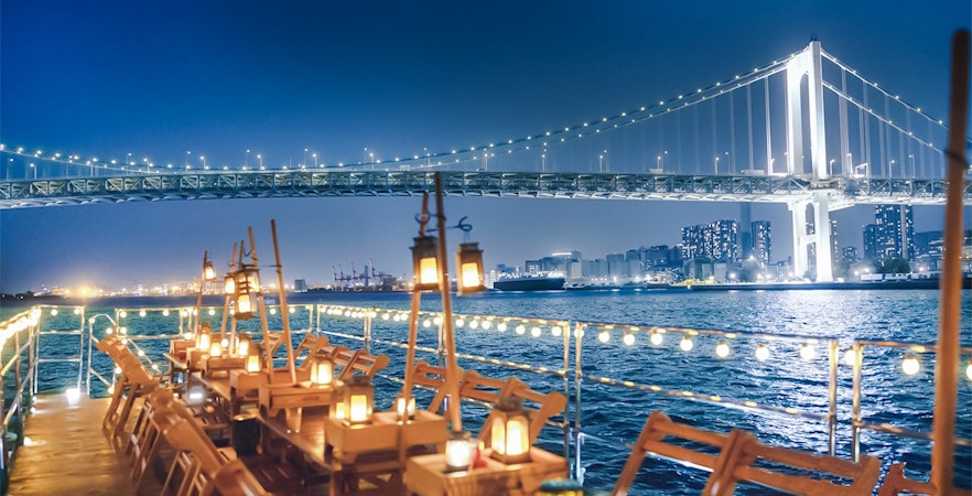 Night view from Yakatabune Cruise deck with illuminated bridge and city skyline in background.