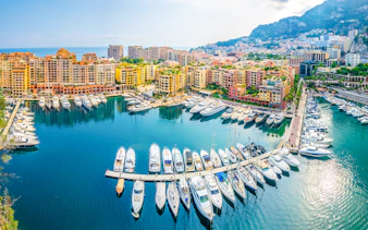 Yachts docked at Port de Fontvieille, Monaco with colorful buildings in the background.