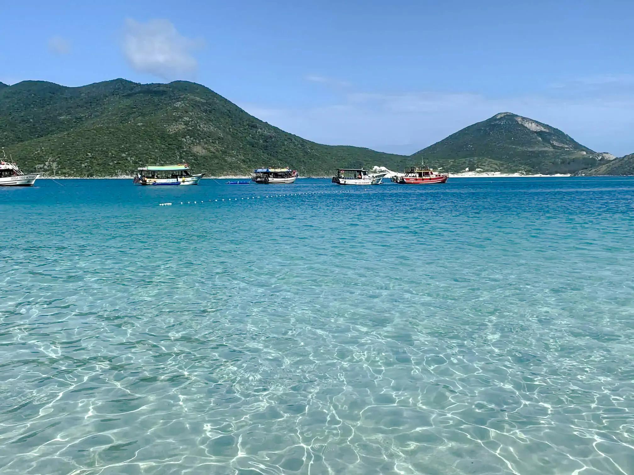 Boats on clear turquoise waters with green hills in Arraial do Cabo, Brazil.