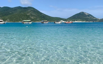 Boats on clear turquoise waters with green hills in Arraial do Cabo, Brazil.