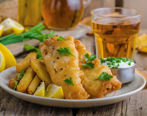 Fish and chips with lemon wedges and tartar sauce on a wooden table.