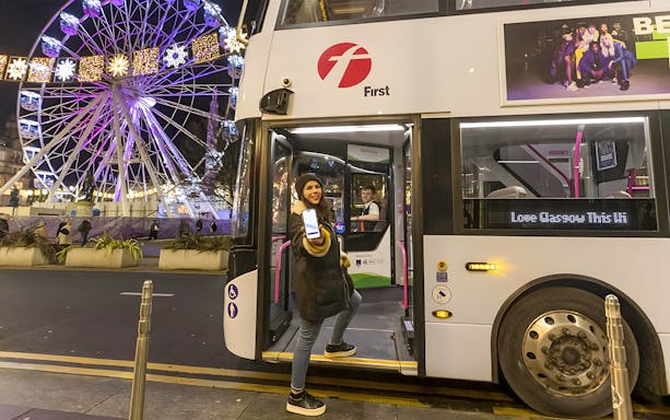 Bus at night in Glasgow with passenger boarding, Ferris wheel in background.