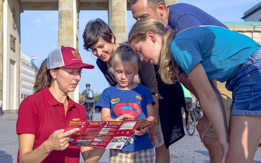 Tour guide showing a map to a family near Brandenburg Gate on Berlin hop-on hop-off bus tour.
