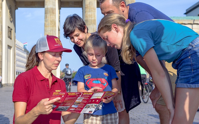 Tour guide showing a map to a family near Brandenburg Gate on Berlin hop-on hop-off bus tour.