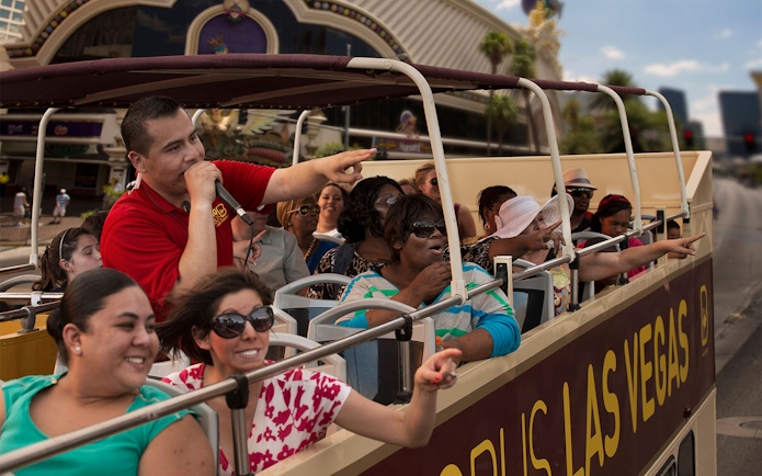 Tourists on Las Vegas hop-on hop-off bus pointing at attractions.