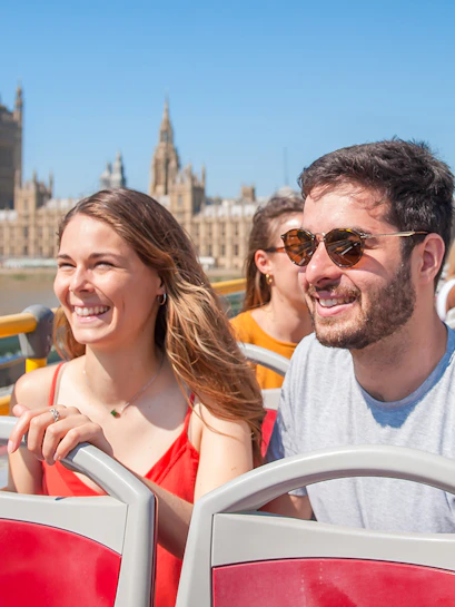 Tourists on a London hop-on hop-off bus with the Houses of Parliament in the background.