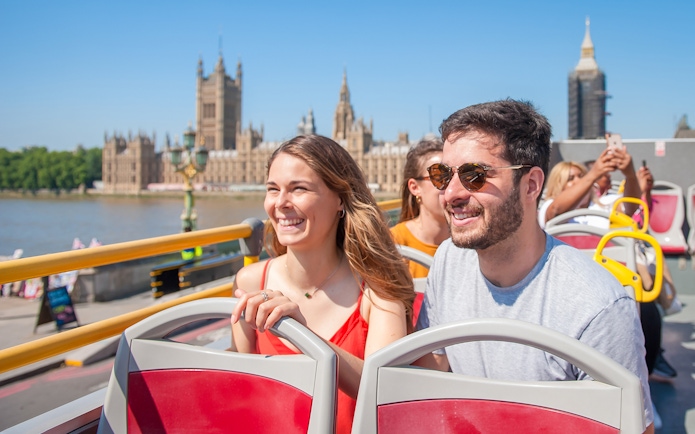 Tourists on a London hop-on hop-off bus with the Houses of Parliament in the background.