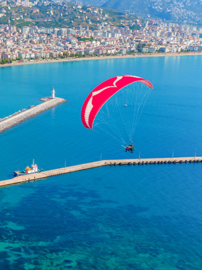 Paragliding over Alanya harbor with cityscape and lighthouse in view.
