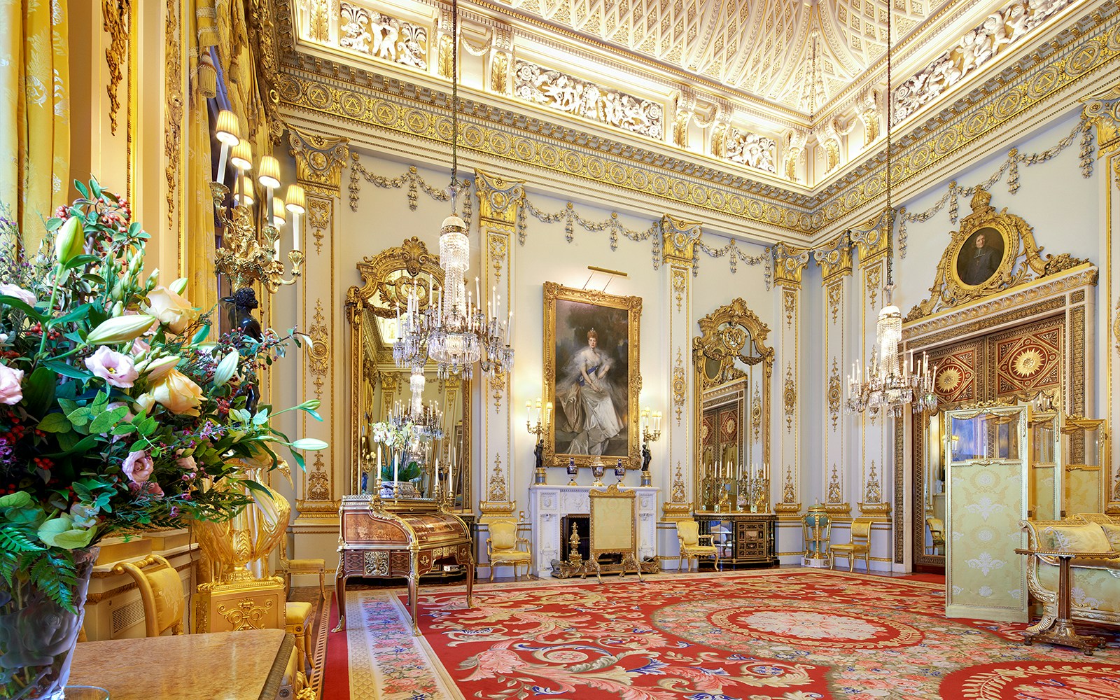 White Drawing Room in Buckingham Palace with ornate gold decor and chandeliers.