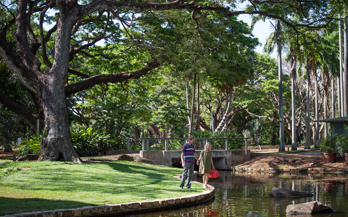 Couple walking by a pond in a lush park during a guided half-day city tour of Darwin.