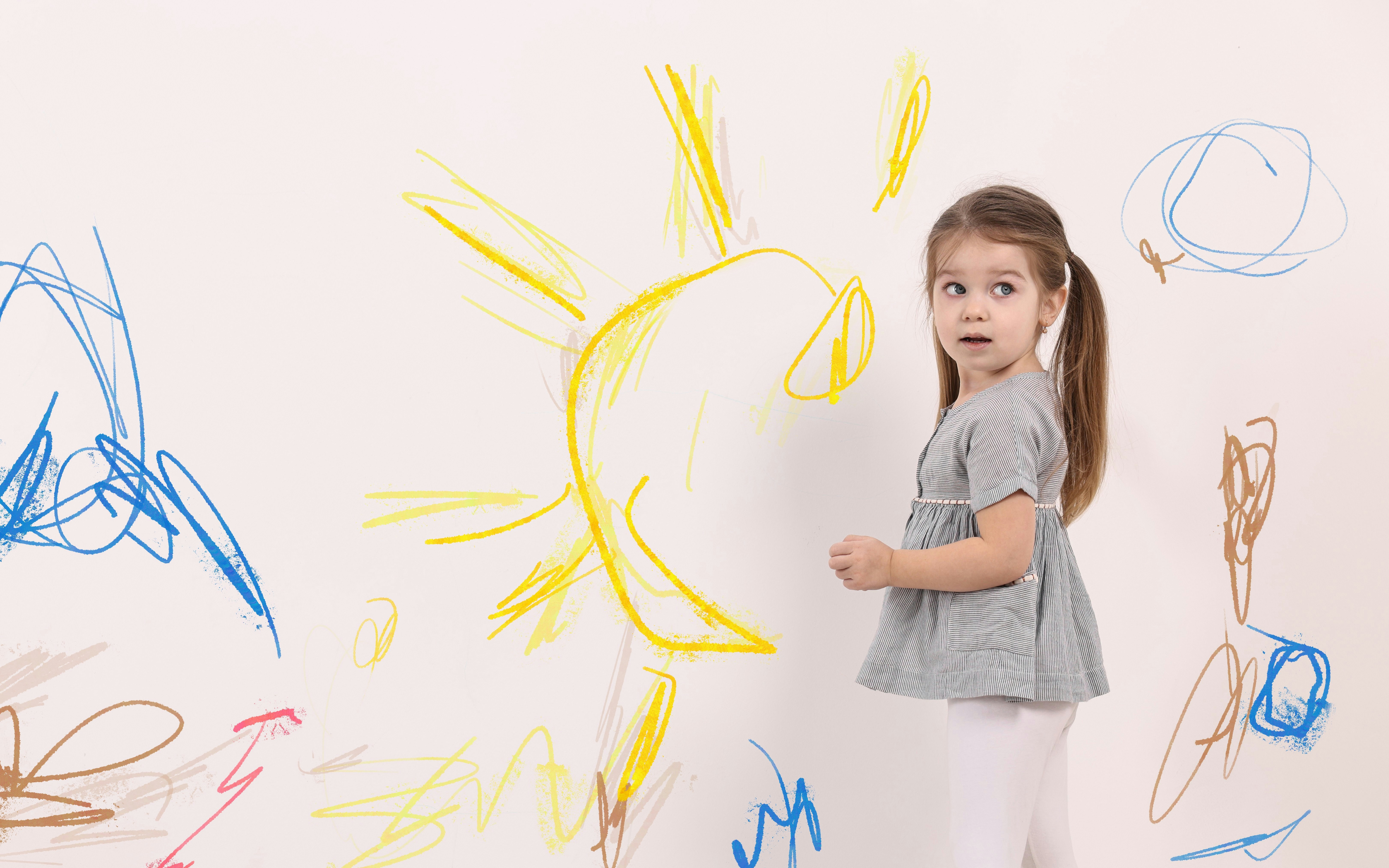 Girl drawing colorful scribbles on a white canvas wall.