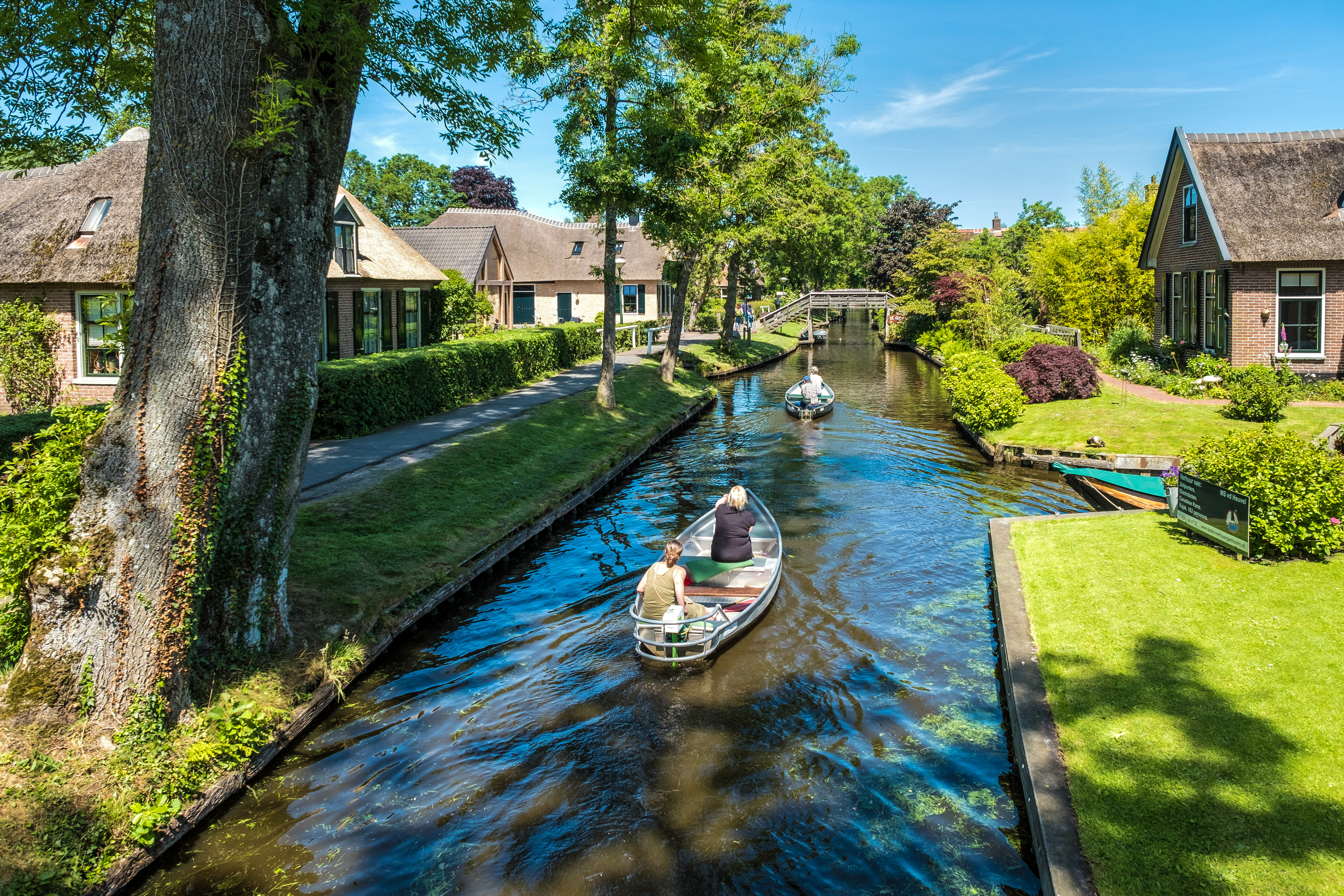 Giethoorn canal with small electric boat and tourists exploring the scenic village on a day tour.