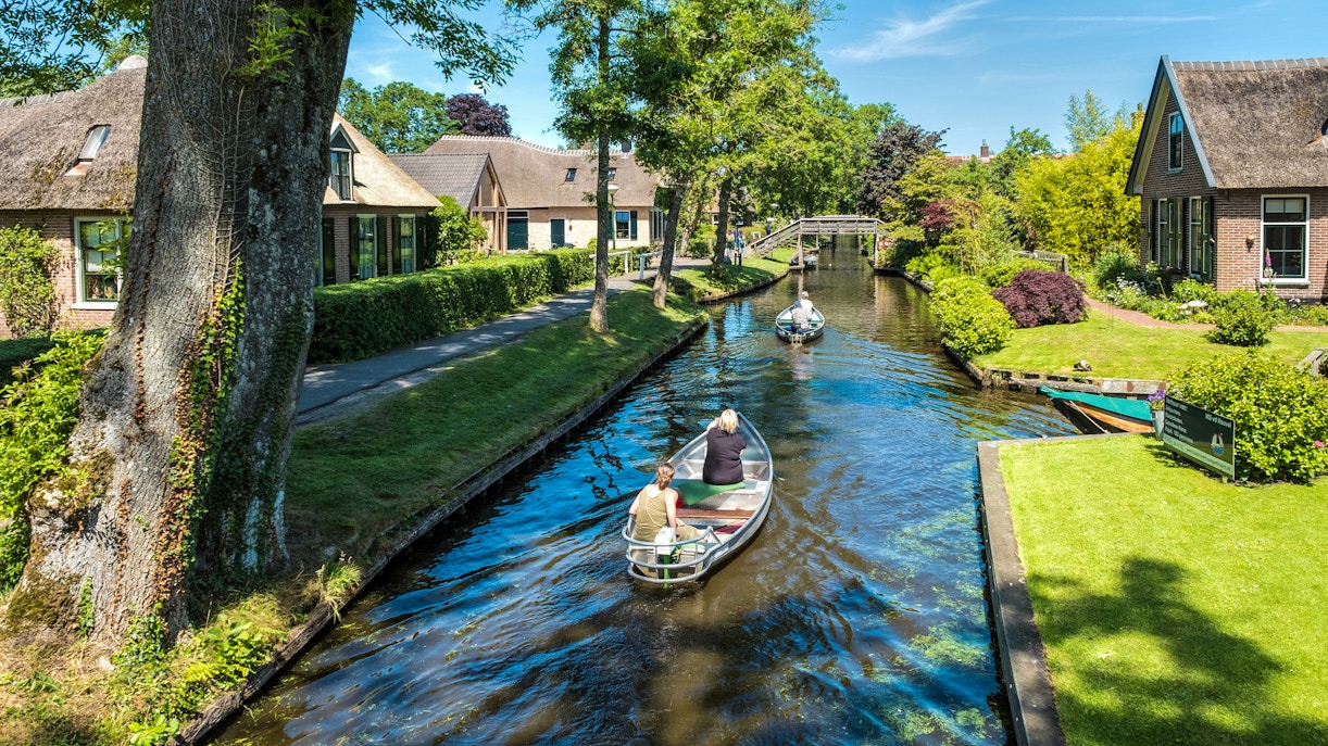 Giethoorn canal with small electric boat and tourists exploring the scenic village on a day tour.