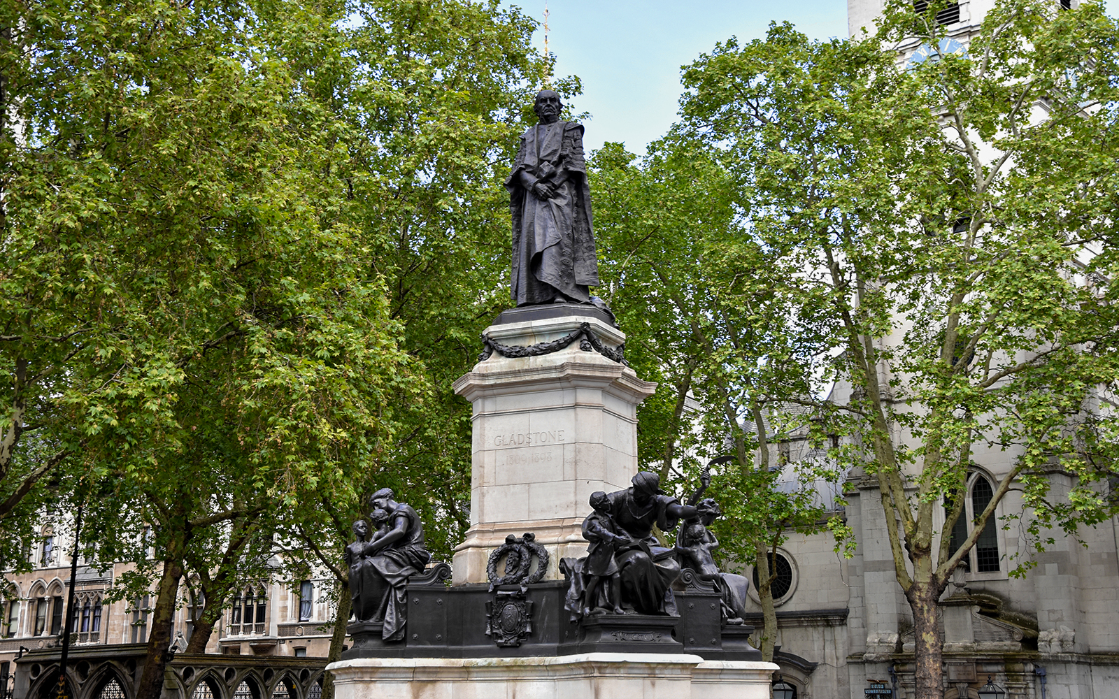 Statue of William Gladstone in London surrounded by trees and historic buildings.