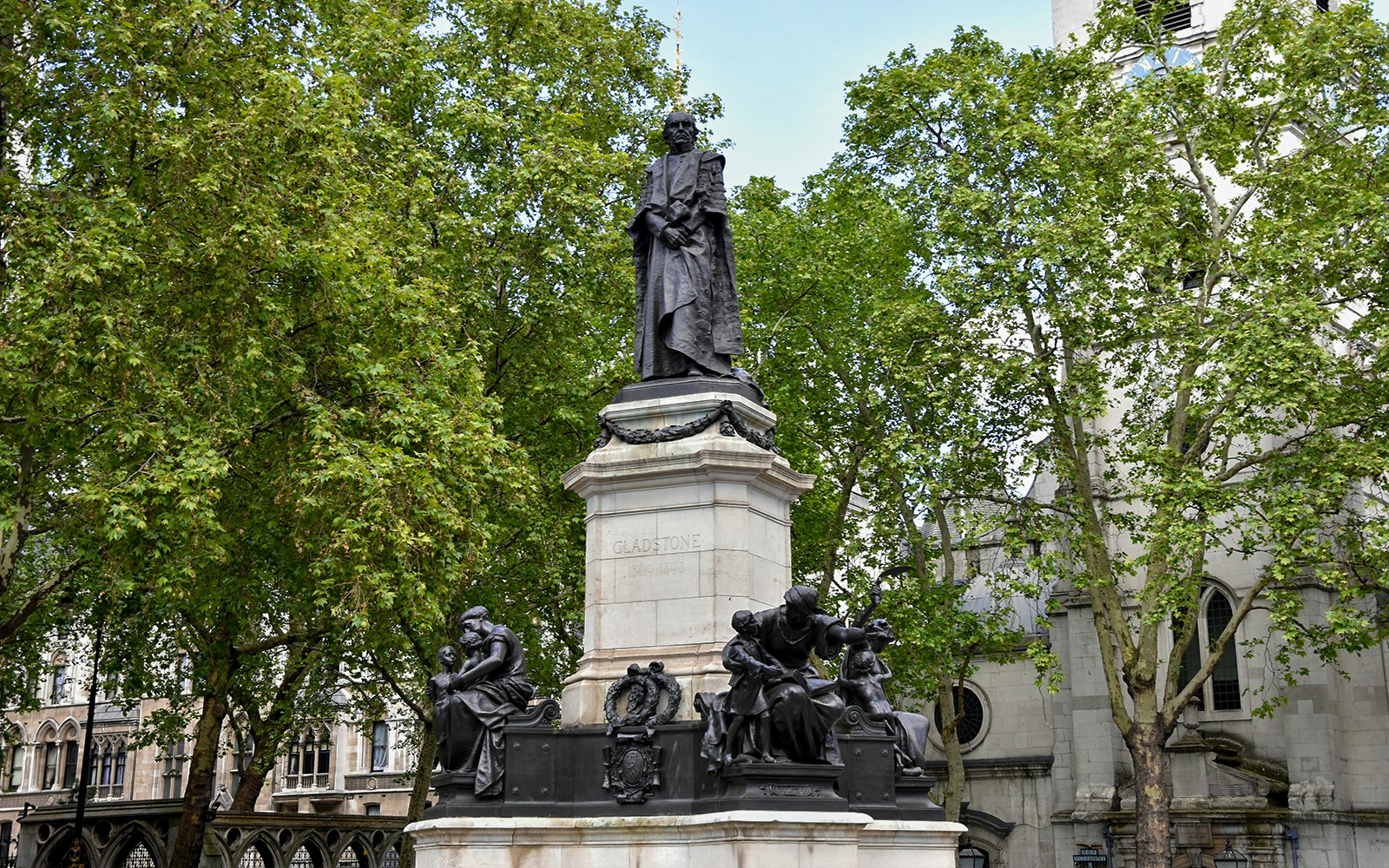 Statue of William Gladstone in London surrounded by trees and historic buildings.