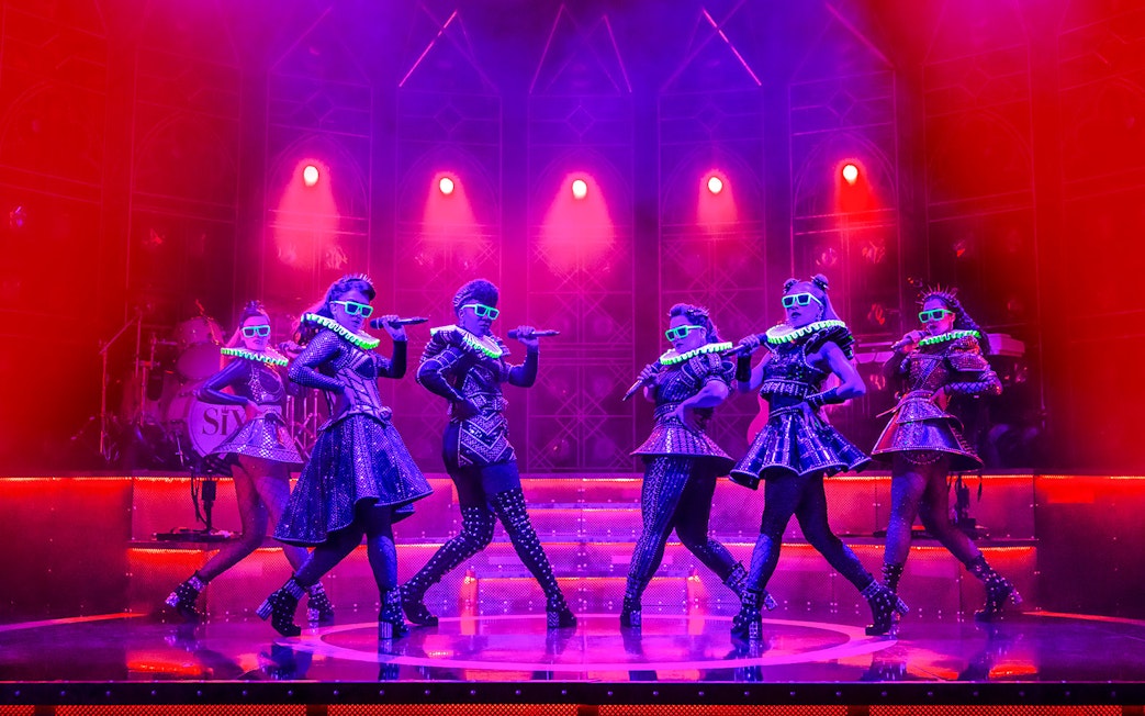 Performers on stage in vibrant costumes during the musical "Six" with dramatic lighting.