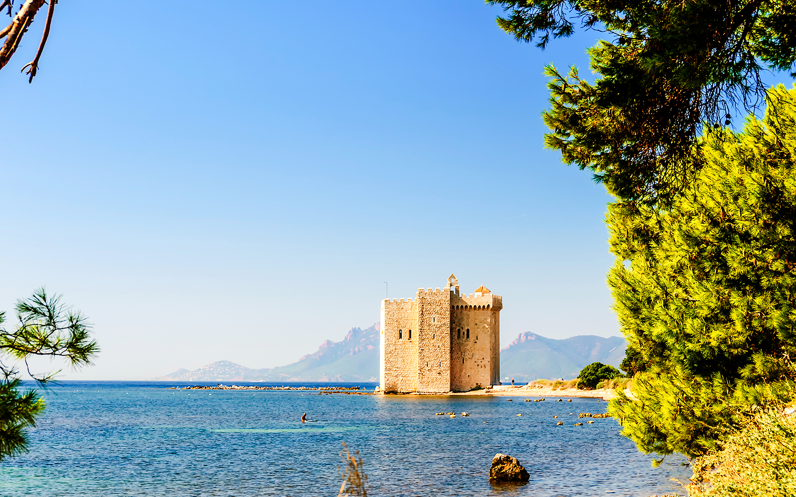 Stone tower on Saint-Honorat Island surrounded by blue sea and distant mountains.