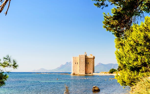 Stone tower on Saint-Honorat Island surrounded by blue sea and distant mountains.