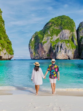 Couple walking on beach at sunrise, Phi Phi Islands, Thailand.