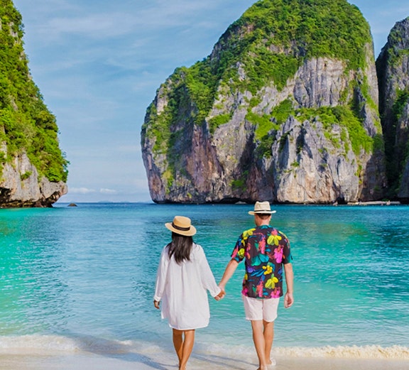 Couple walking on beach at sunrise, Phi Phi Islands, Thailand.