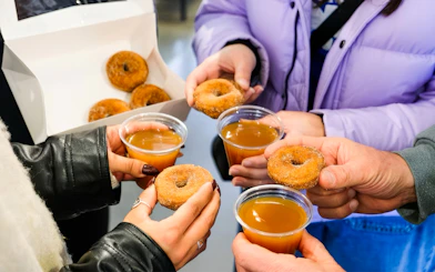 Hands holding donuts and cider during a guided tasting tour in Boston.