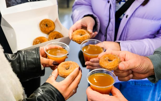 Hands holding donuts and cider during a guided tasting tour in Boston.