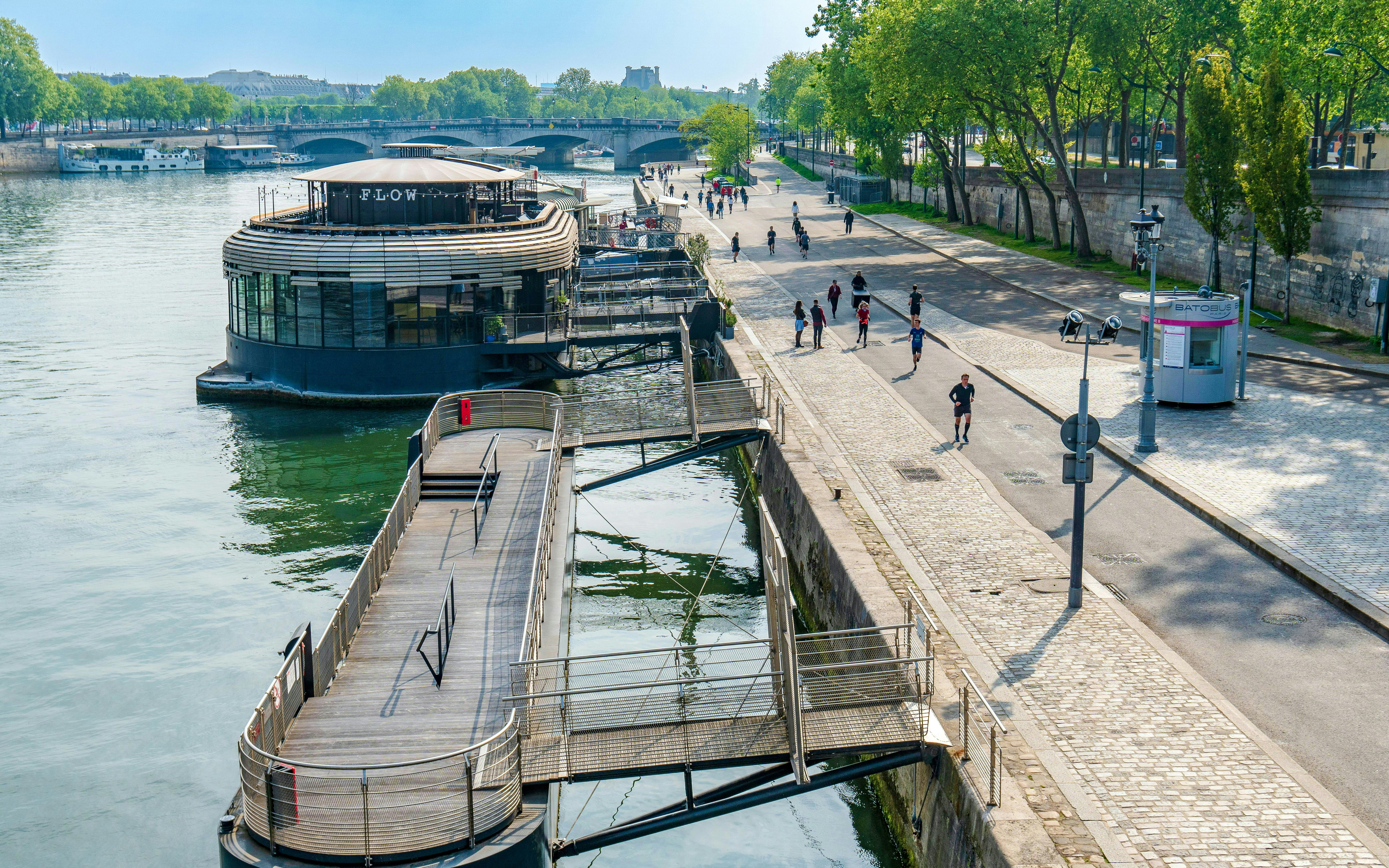 Seine riverfront with people walking and a docked boat restaurant in Paris.