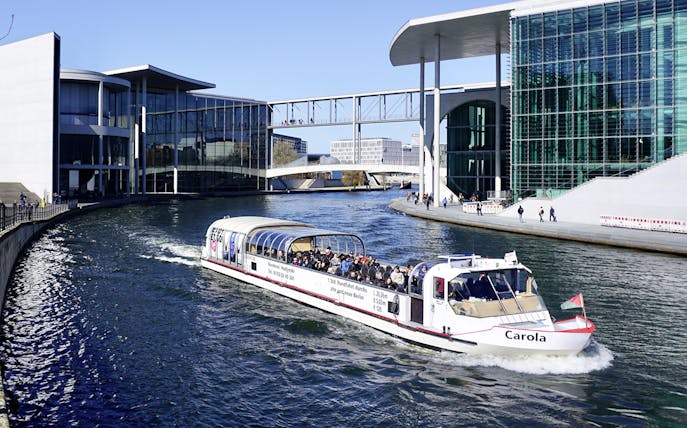 River cruise boat with tourists near modern buildings in Berlin.