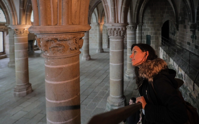 Visitor exploring the interior columns of Mont St. Michel's Abbey during a full day tour from Paris.