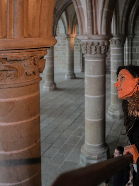 Visitor exploring the interior columns of Mont St. Michel's Abbey during a full day tour from Paris.