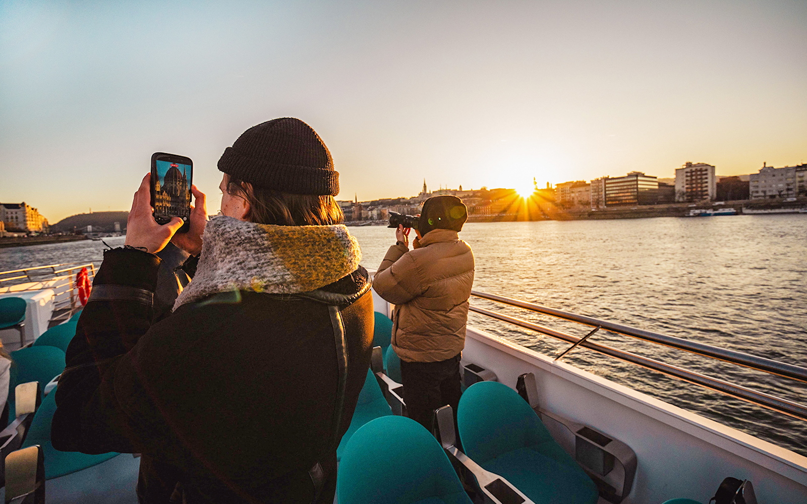 Guests photographing sunset on Budapest cruise with city skyline in view.