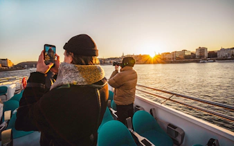 Guests photographing sunset on Budapest cruise with city skyline in view.