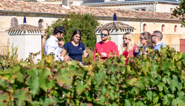 People on Wine tasting tour during Saint-Emilion vineyard with wine barrels and historic village in the background.